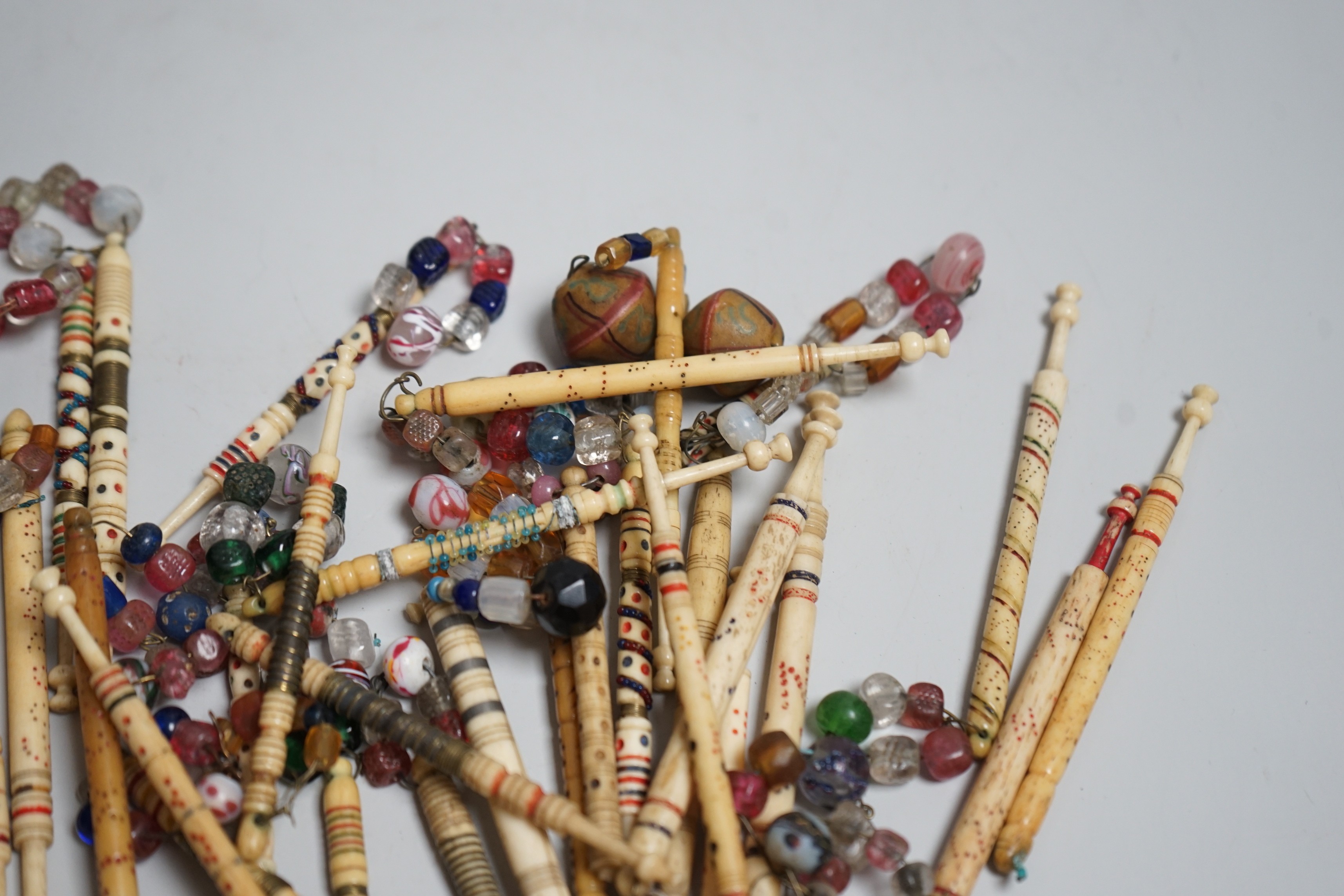 Twenty 19th century ornately decorated lace bobbins with glass bead tops and eleven carved bobbins with indistinctly carved surnames and names